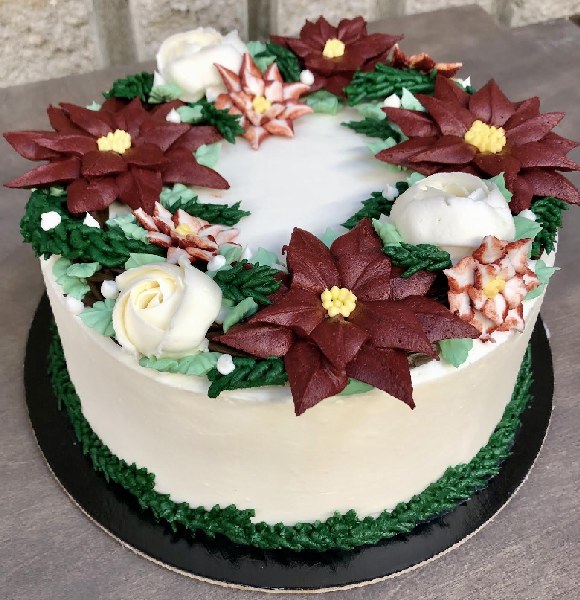 Round stacked cake in white icing with green trim and icing pointsettias and flowers.