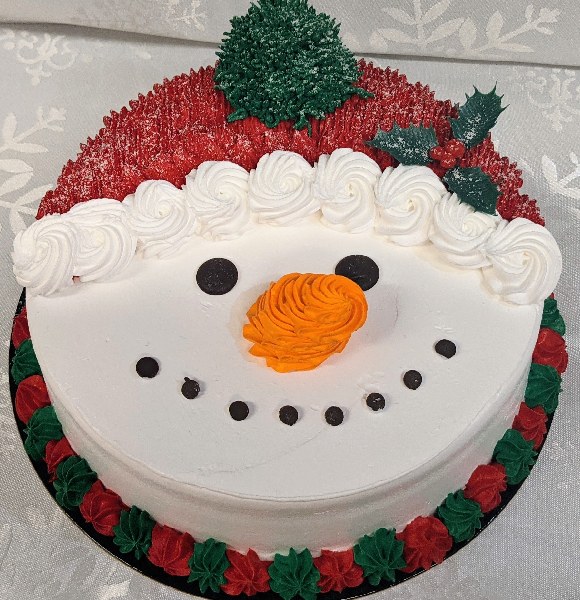 Round snowman head cake with carrot nose, coal mouth and eyes and wearing Santa hat.