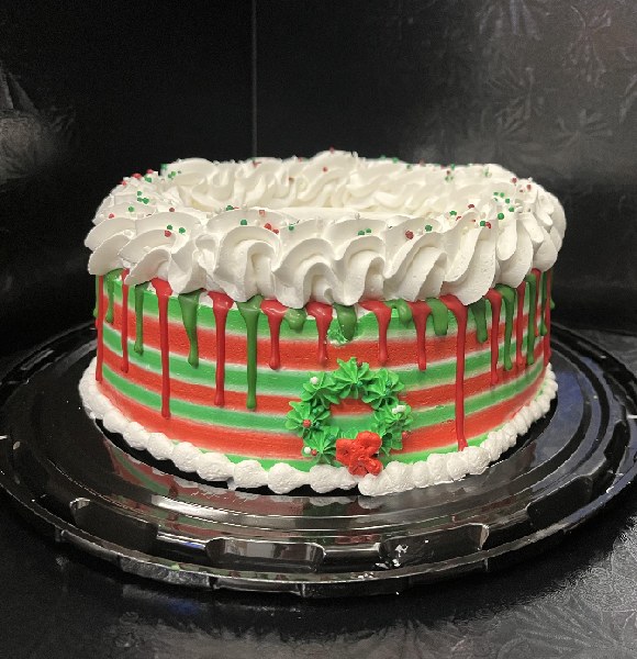 Round cake with green and red stripes. White trim on bottom and thick white icing trim on the top with Christmas wreath on the side.