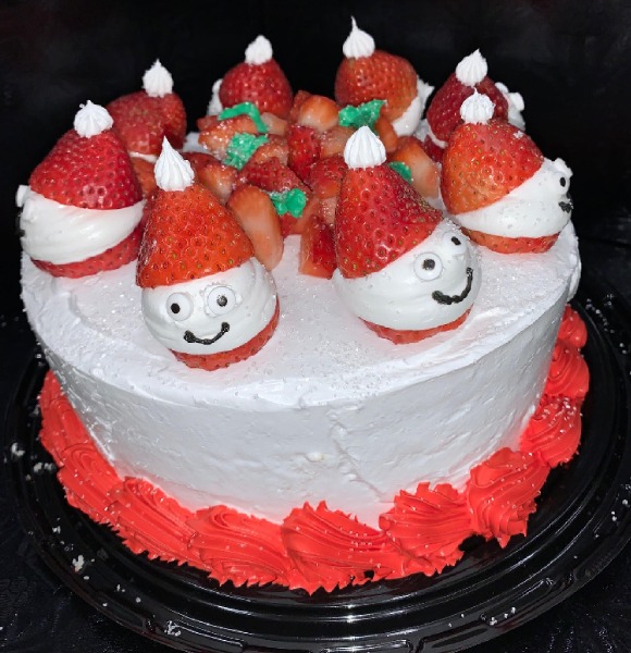 Round cake in white icing with red trim on bottom with snowman heads with Santa hats on top.