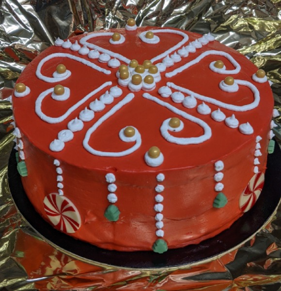 Round stacked cake on silver background covered in red icing with white candy cane decorations and trim and green dots.