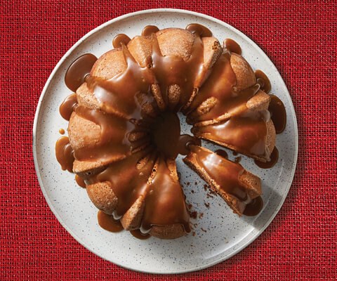 A round plate with a baked gingerbread bundt cake topped with a sauce.