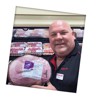 Mike Dillabough of Eganville Foodland stands in front of store's refridgerated sausage section and holds a ham.