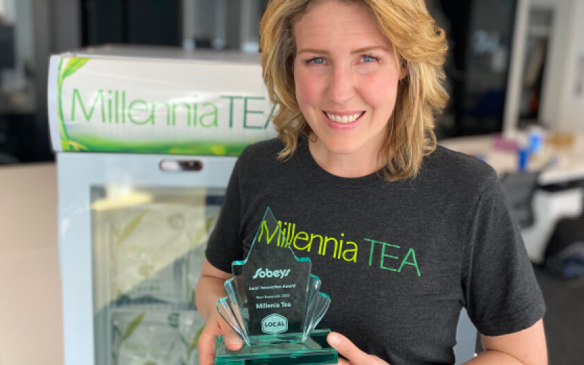Tracy Bell of Millenia Tea holding a glass award wearing a company branded black t-shirt.