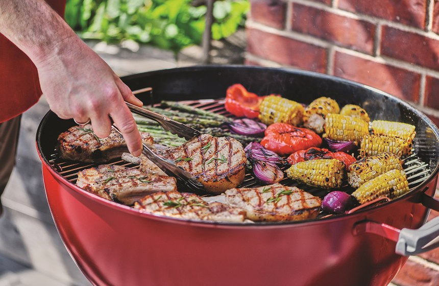 Pork chops on grill with corn, onions, and peppers on the side