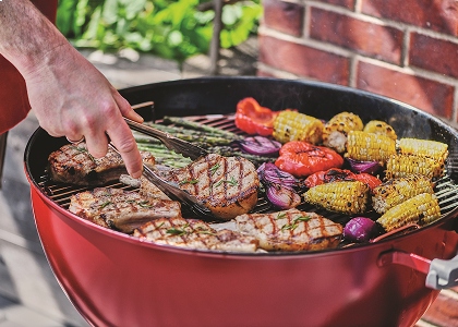 Pork chops on grill with corn, onions, and peppers on the side