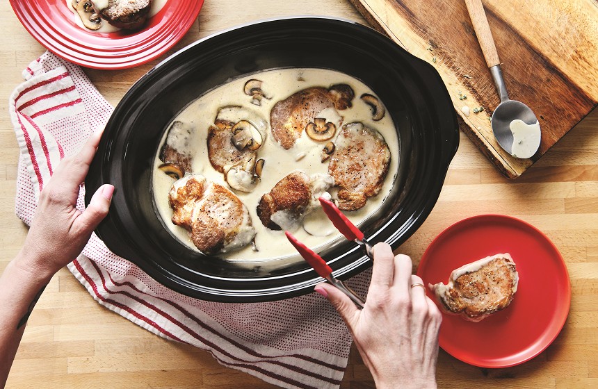 Pork in creamy sauce being transferred from slow cooker to plate.