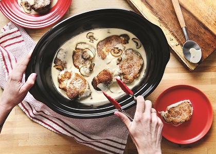 Pork in creamy sauce being transferred from slow cooker to plate.