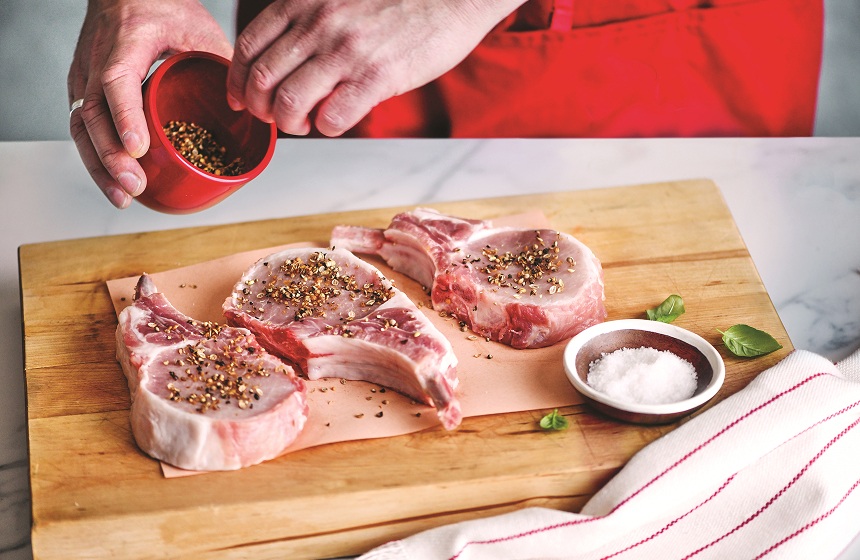 Man adding spice rub to raw pork chips on cutting board