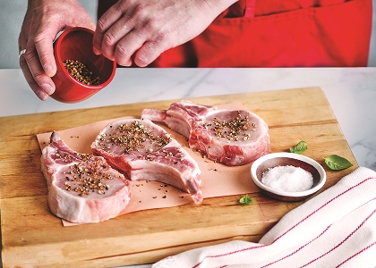 Man adding spice rub to raw pork chips on cutting board