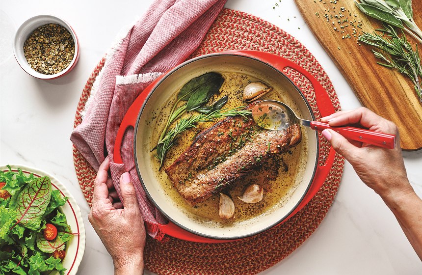Overhead shot of pork in plate being basted in butter and herb sauce