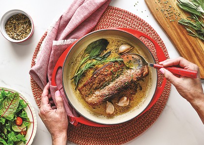 Overhead shot of pork in plate being basted in butter and herb sauce